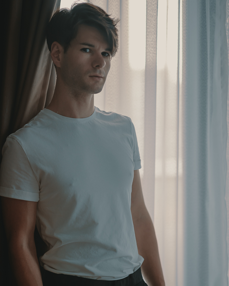portrait of zaccy in a plain white t-shirt standing in front of a window